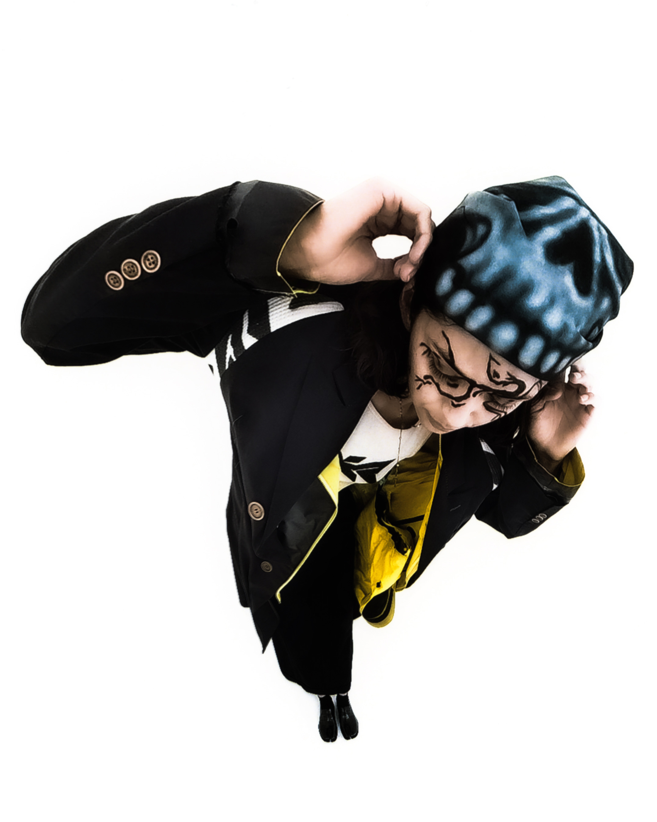 Ariel shot of a model wearing black graphic liner, a long black coat and bandana against a white background